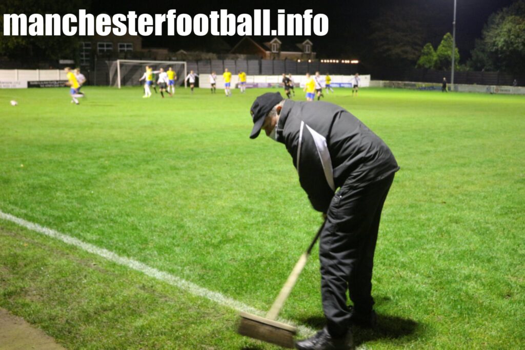 Mossley club official Steve Tague sweeping glass from the pitch after a floodlight bulb exploded